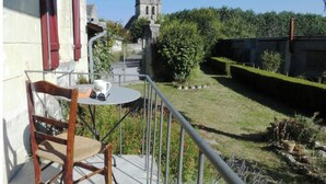 A balcony with a chair and table, overlooking a church and a well-maintained garden. - Le Dorelot du lièvre, house of character (Seuilly)