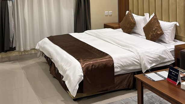 A hotel room with a large bed, a wooden headboard, a nightstand, and a desk with a chair. - luluat althuraya serviced apartmints 8 (Riyadh)