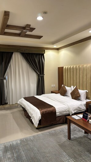 A hotel room with a large bed, a wooden headboard, a nightstand, and a desk with a chair. - luluat althuraya serviced apartmints 8 (Riyadh)