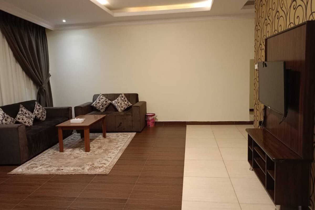 A living room with a sofa, a coffee table, a TV, and a patterned wall.