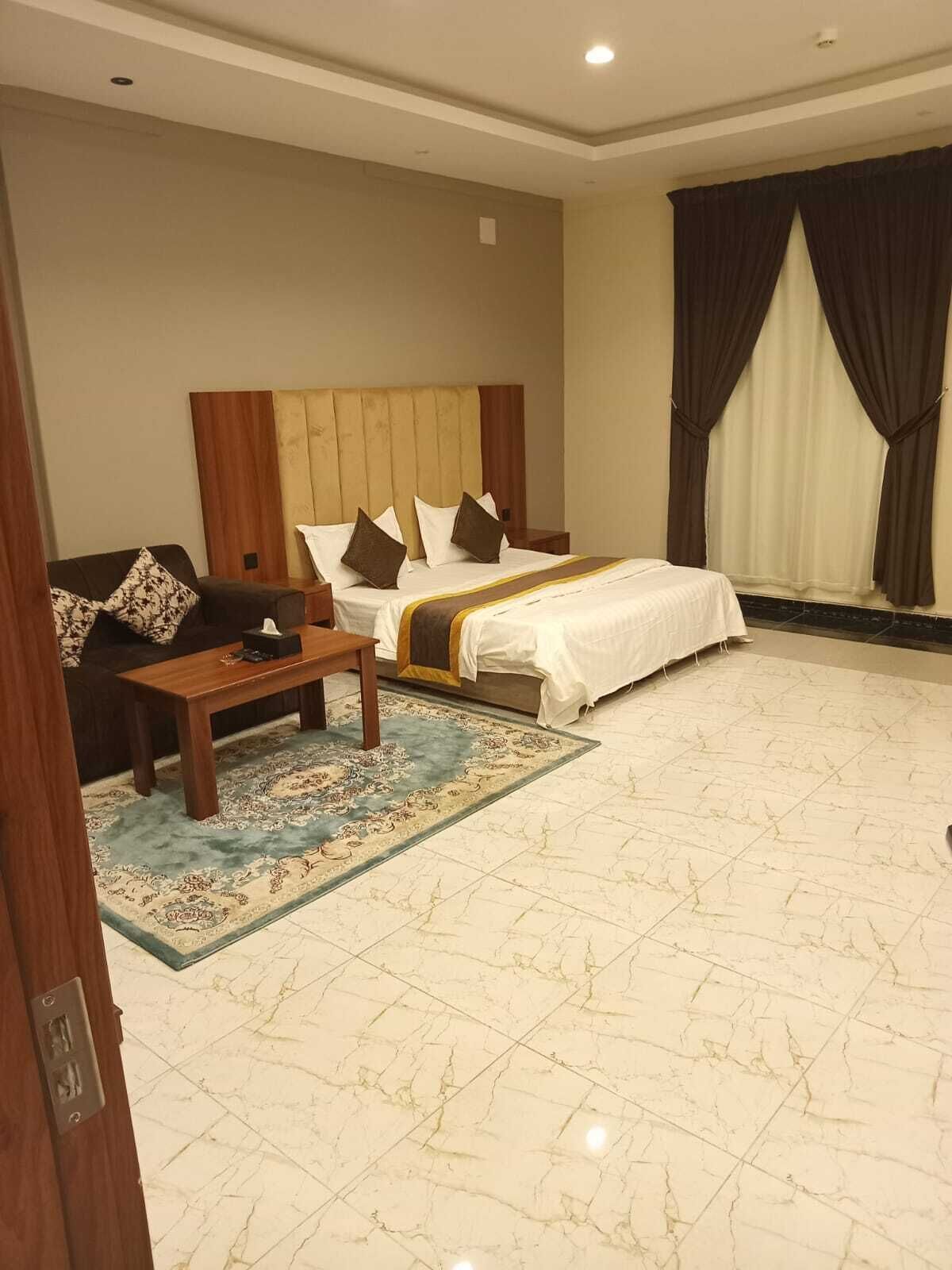 A hotel room with a bed, a sofa, a coffee table, and a patterned rug.