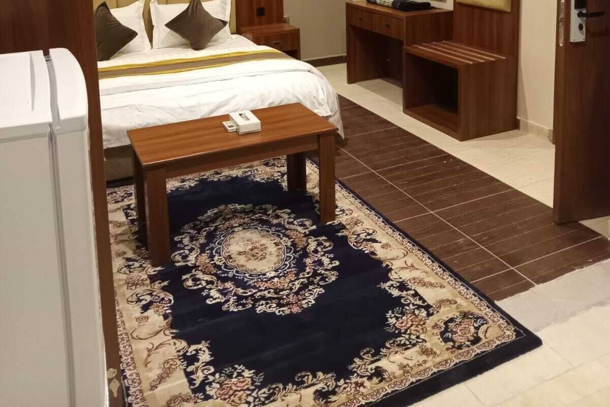 A hotel room with a bed, bedside tables, a desk, a mirror, and an air conditioning unit.