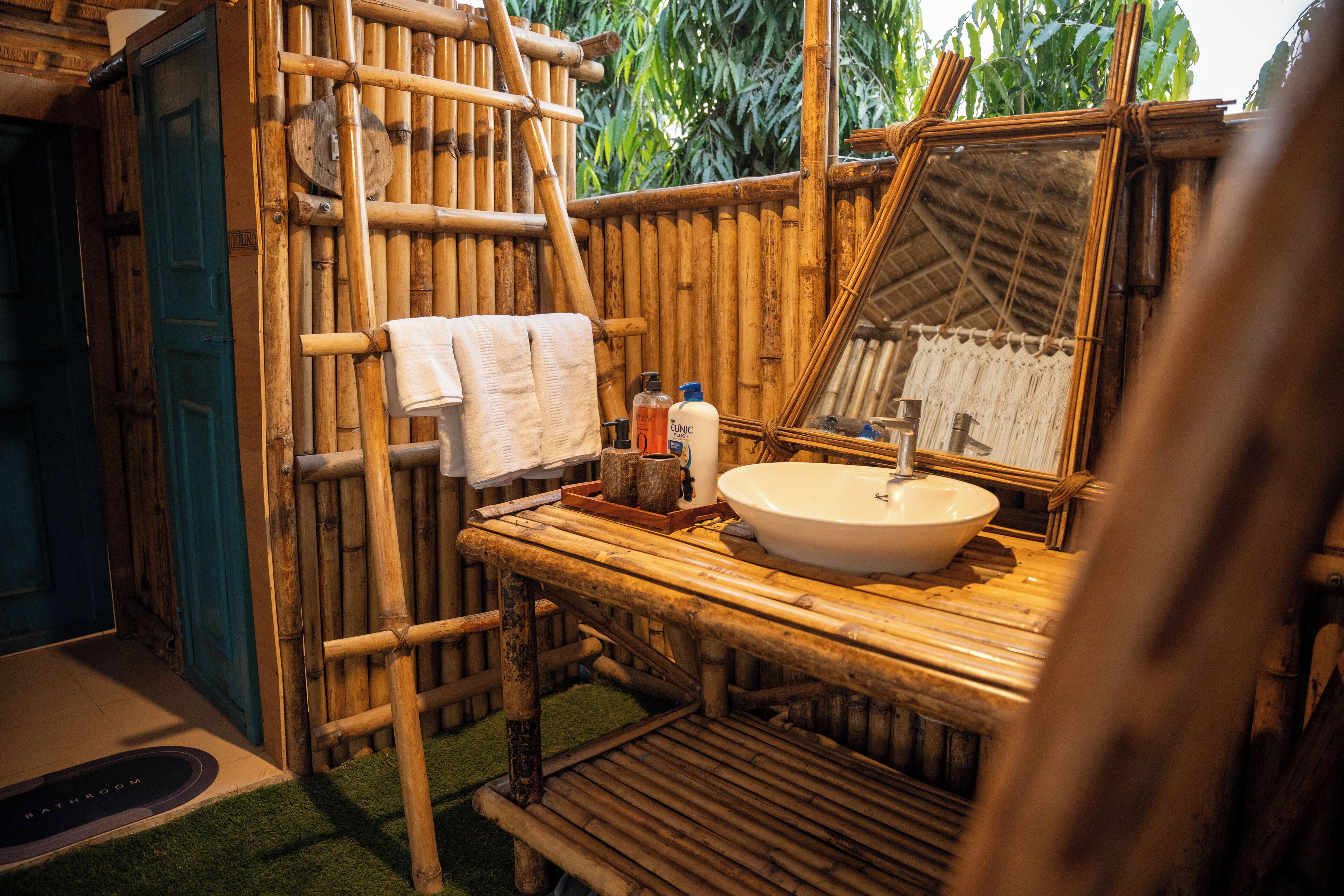 Une salle de bain décorée sur le thème du bambou, avec un lavabo, un miroir et des articles de toilette.