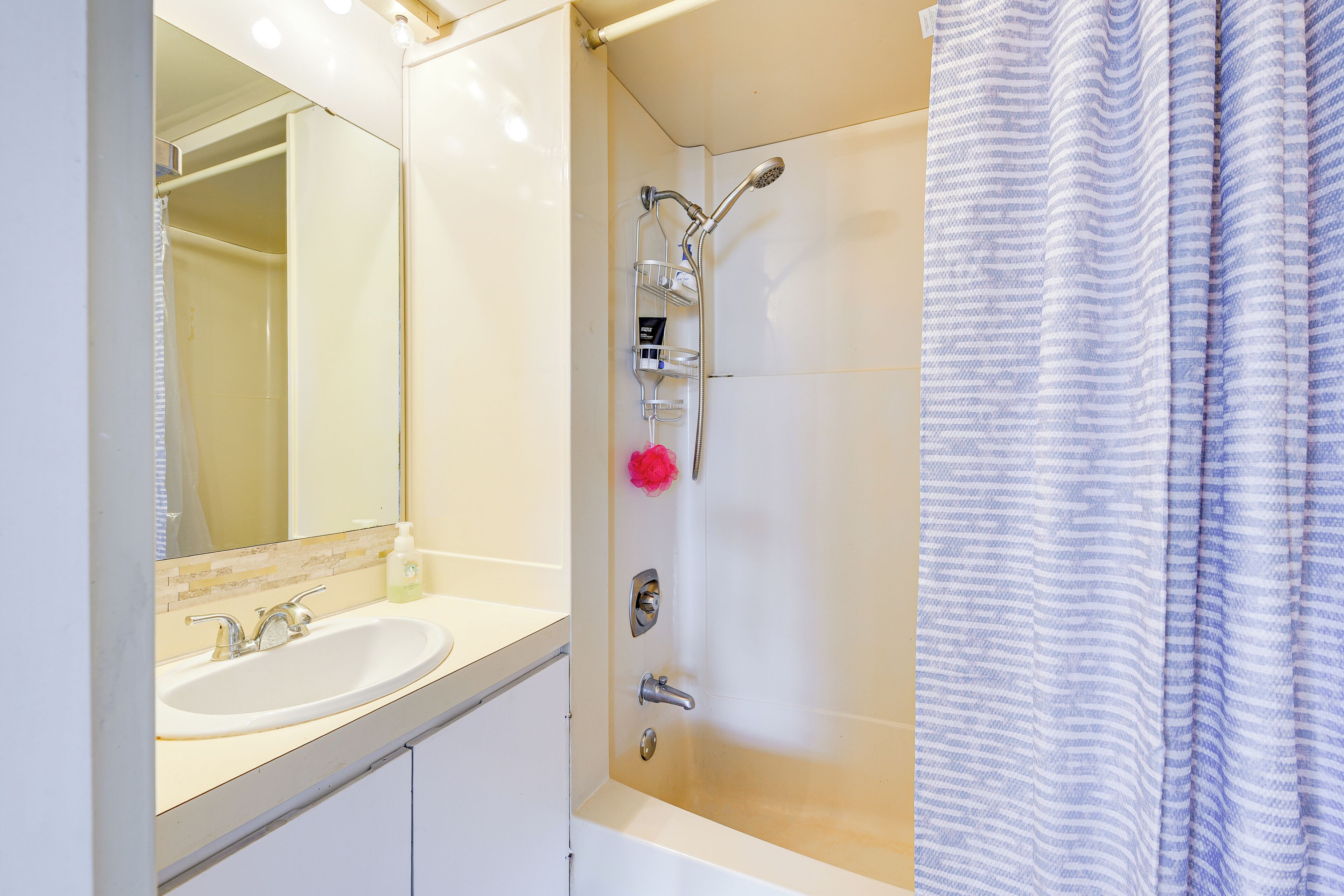 Ein Badezimmer mit Waschbecken, Spiegel, Dusche und Handtuchhalter.