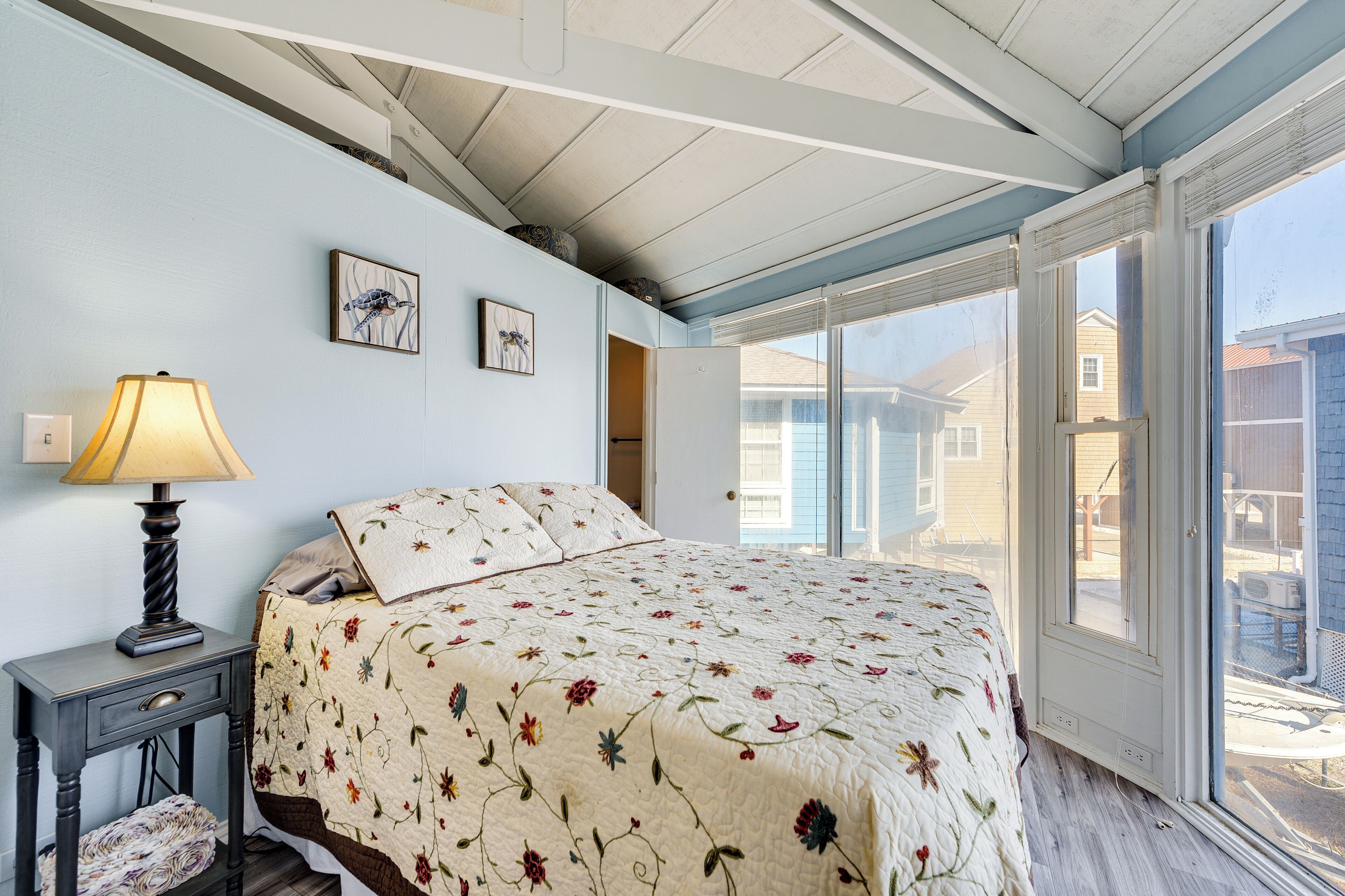 A bedroom with a bed, a nightstand, a lamp, and a window with a view of the outside.