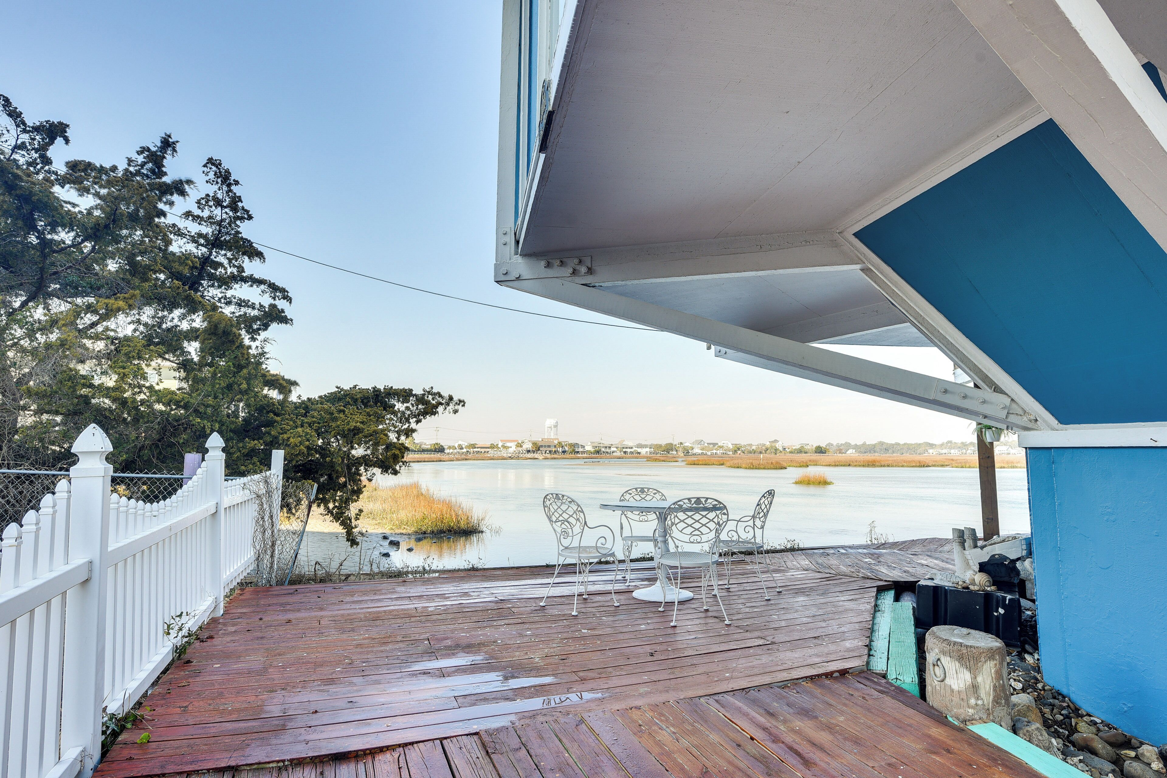 Una terraza de madera con cerca blanca, una mesa con sillas y vista a un cuerpo de agua.