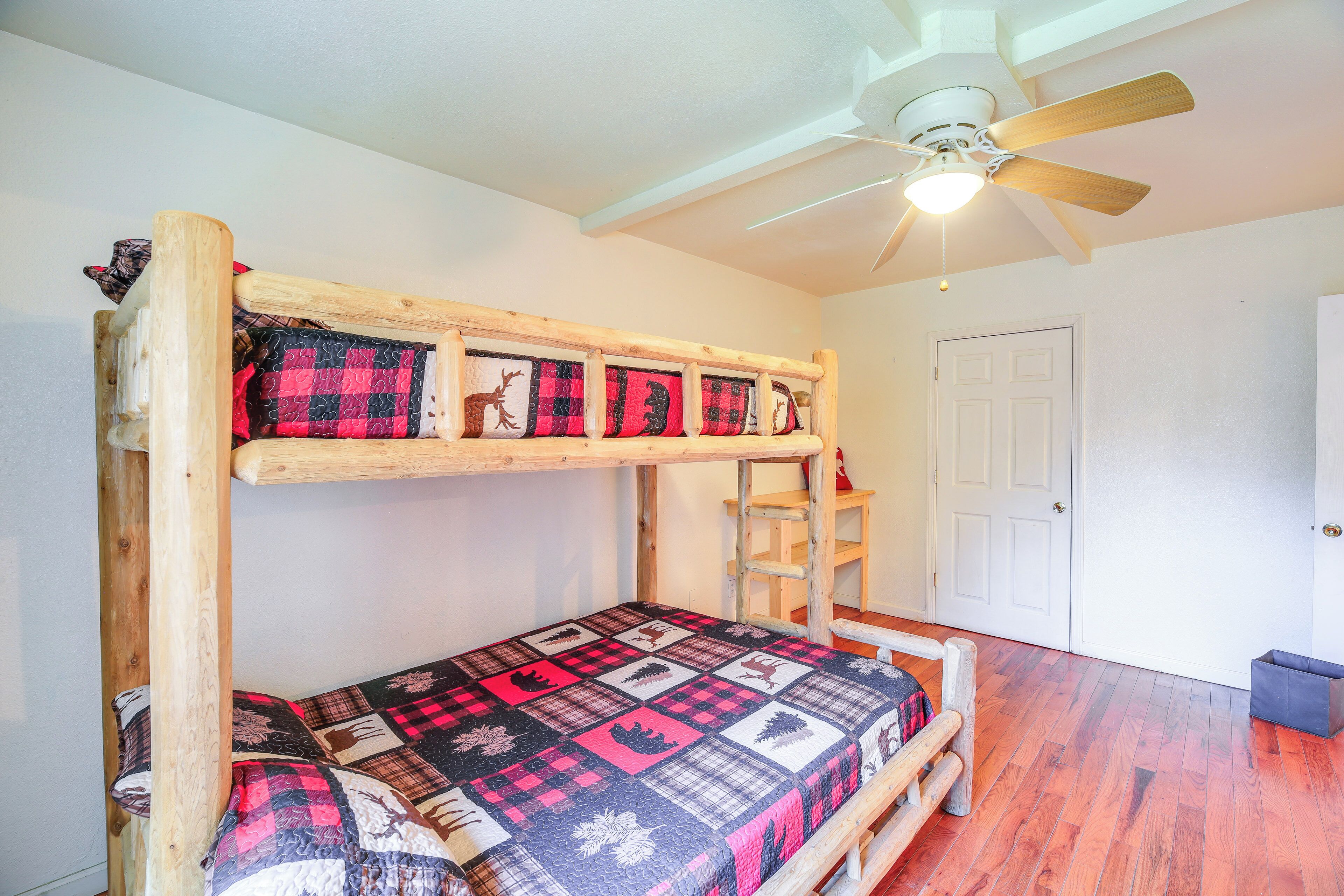 A bunk bed with a quilted bedspread, a ceiling fan, and a door in a room with wooden flooring.