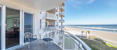 A balcony with a view of the beach, a dining area with chairs, and a living room with a sofa.