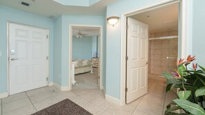 A hallway with two white doors, a bedroom with a bed and dresser, and a bathroom with a shower.