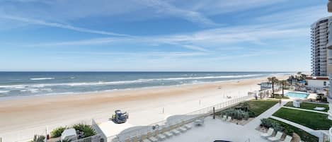 A beachfront hotel with a pool, lounge chairs, and a view of the beach and ocean.