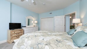 A bedroom with a bed, dresser, TV, and a door leading to another room.