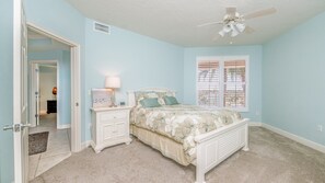 A bedroom with a bed, nightstands, a ceiling fan, and a window with blinds. - 306 St Maarten - Oceanfront Paradise (Daytona Beach Shores)