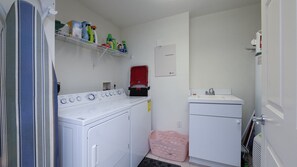 A compact laundry room with a front-loading washer and dryer, a small sink, and shelves with cleaning supplies.
