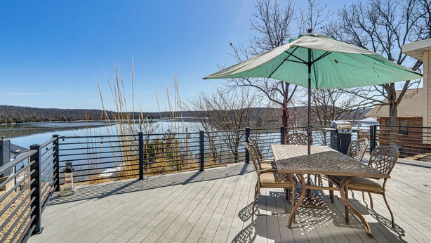 A wooden deck with a table and chairs, a green umbrella, and a view of a lake.