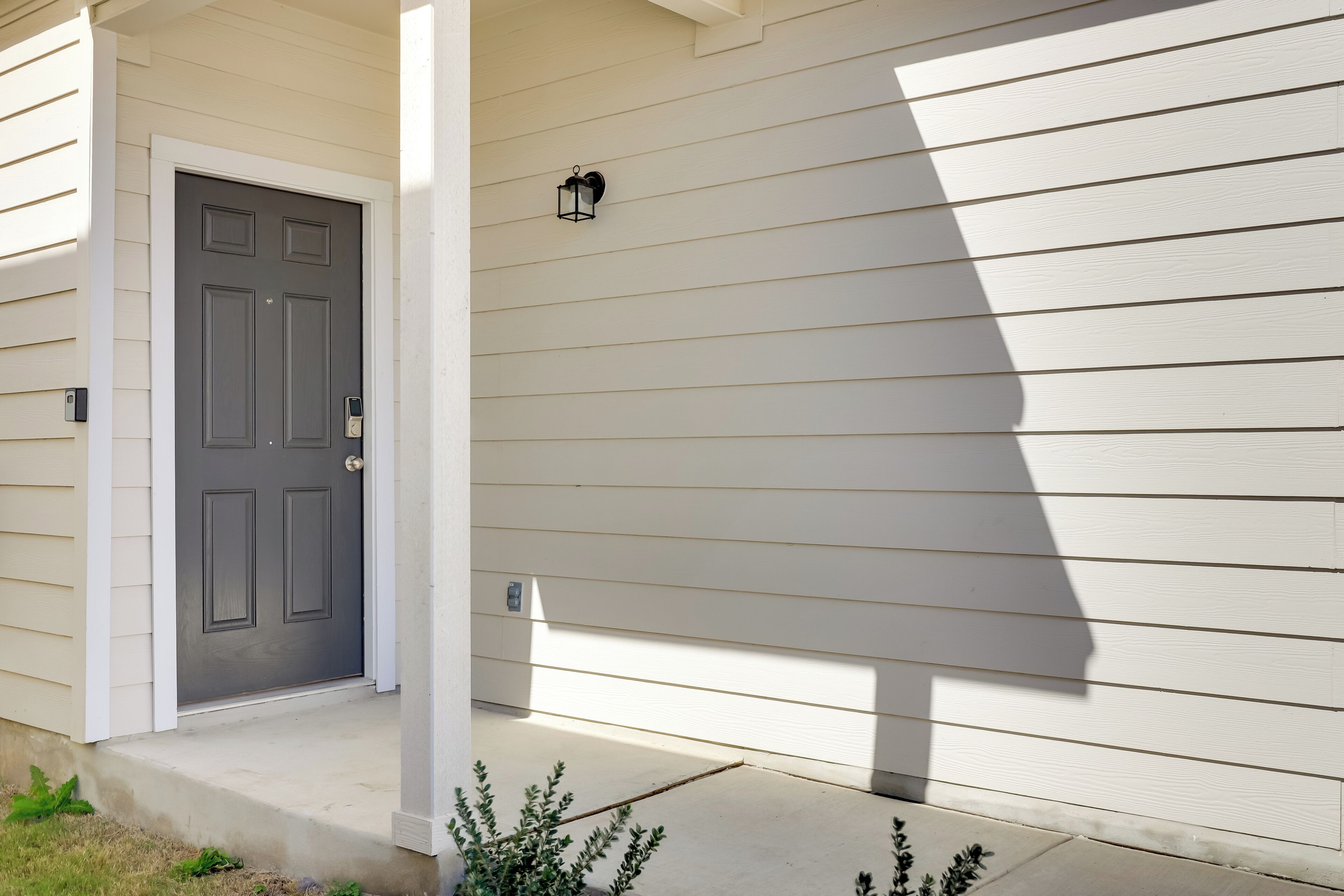 A house with a gray front door, a small porch, and a wall-mounted light fixture.