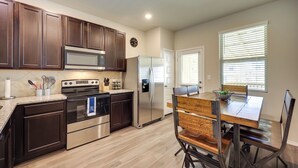 Une cuisine moderne avec des meubles en bois foncé, des appareils électroménagers en acier inoxydable et un coin repas comprenant une table et des chaises en bois.