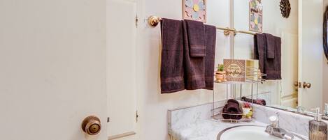 A bathroom with a white sink, a mirror, and a towel rack with multiple towels.
