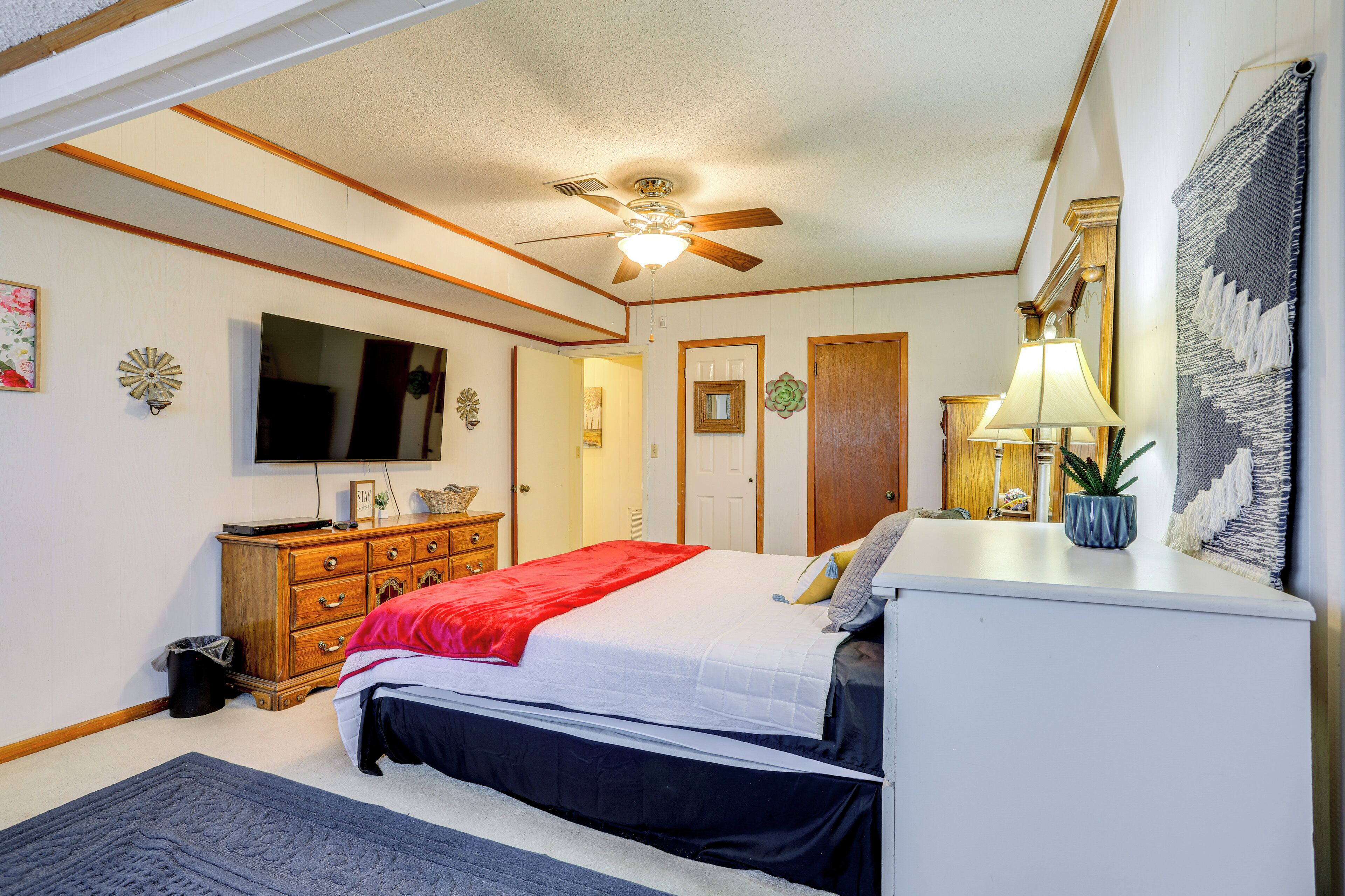 A bedroom with a bed, dresser, ceiling fan, TV, and a small plant.
