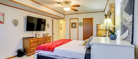 A bedroom with a bed, dresser, ceiling fan, TV, and a small plant.