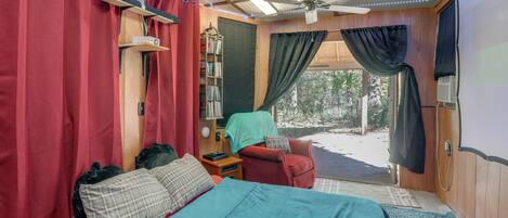 Un dormitorio acogedor con cama, un escritorio pequeño, una silla, una estantería y una ventana con cortinas.