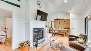 Una sala de estar con chimenea, televisor montado en la pared y comedor con pared de ladrillo y muebles de madera.