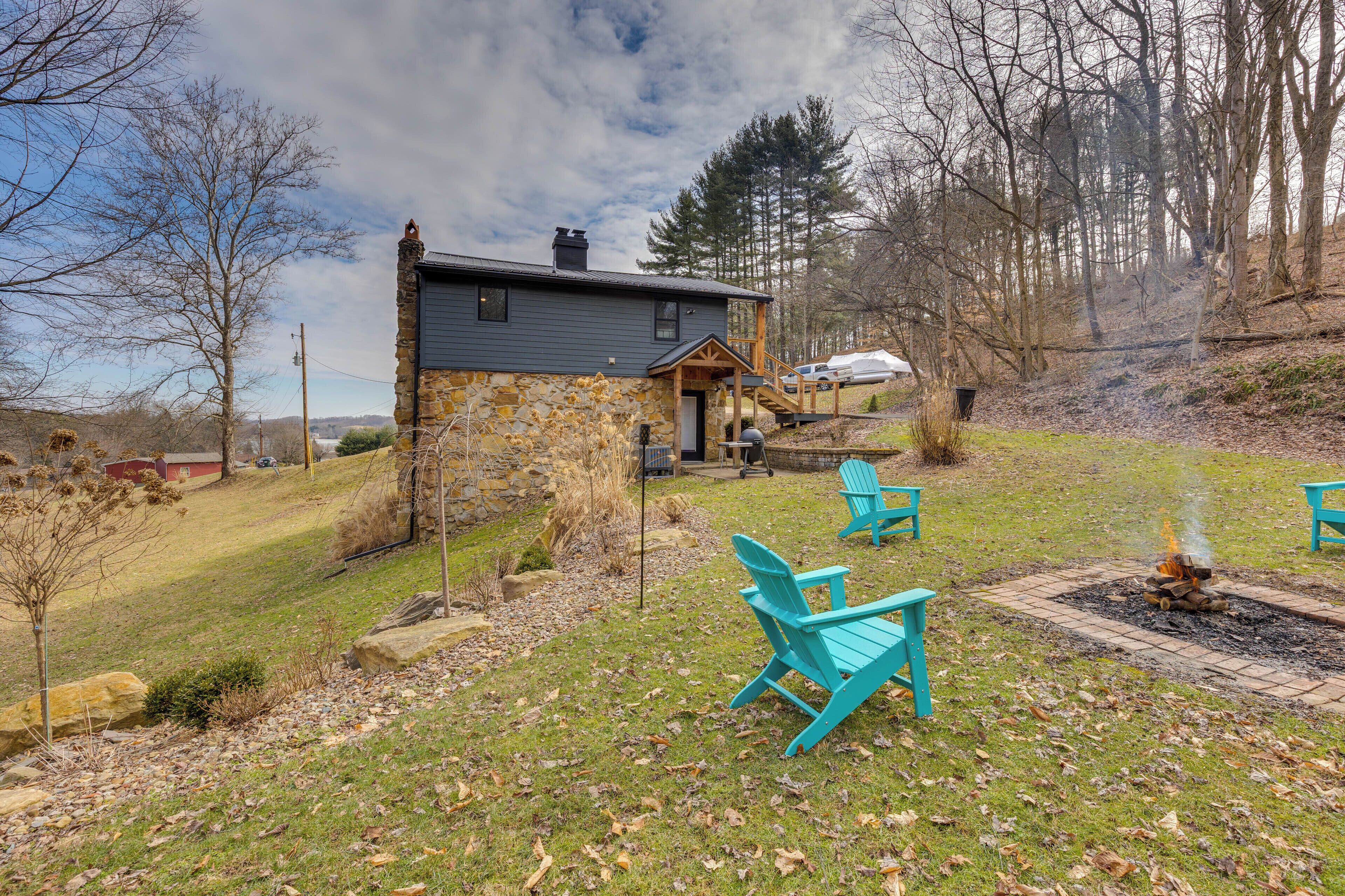 A stone house with a porch, two turquoise Adirondack chairs, and a fire pit.