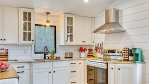 Una cocina moderna con armarios blancos, electrodomésticos de acero inoxidable y un ventanal sobre el fregadero.