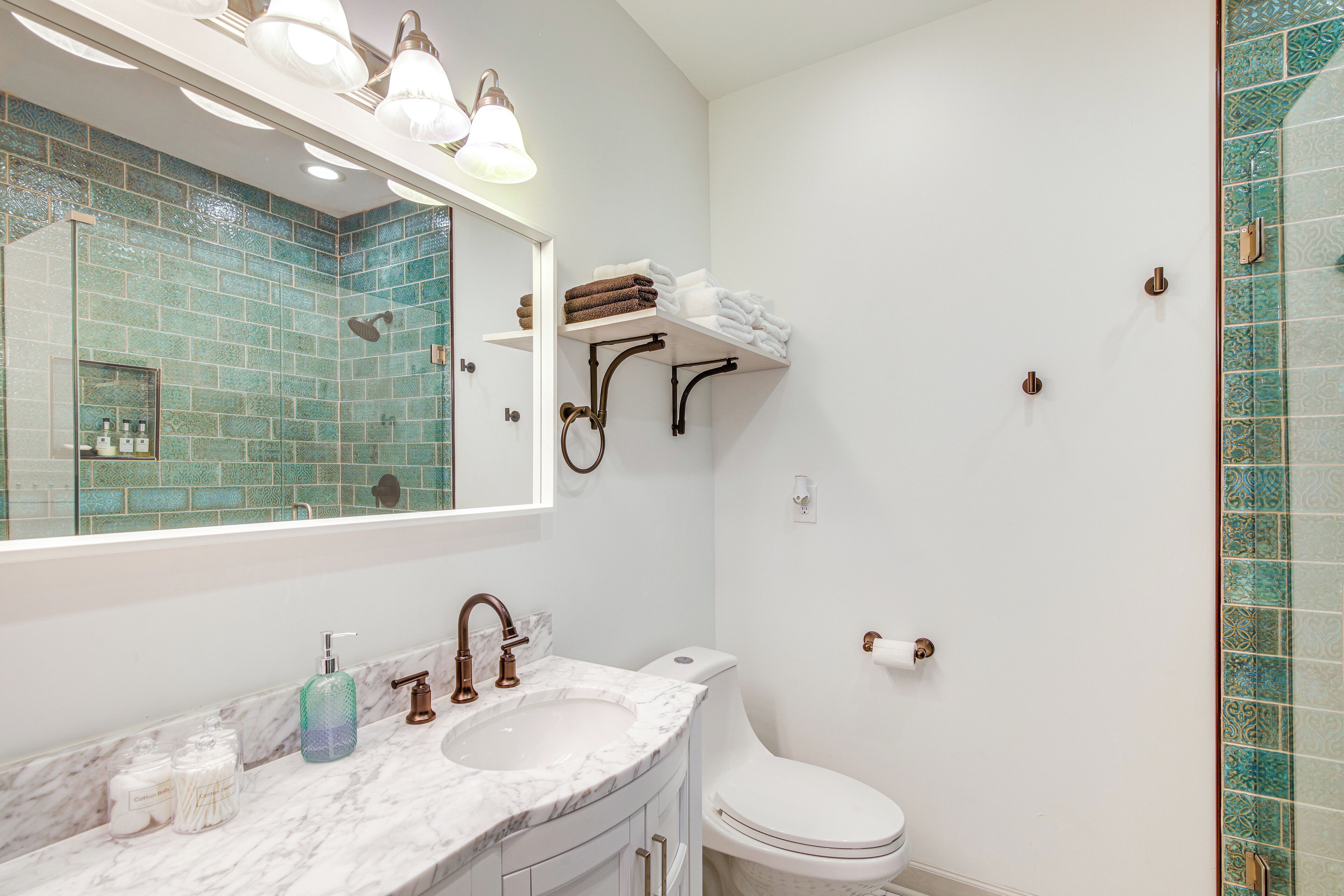 A bathroom with a marble sink, white toilet, and a mirror with lights.
