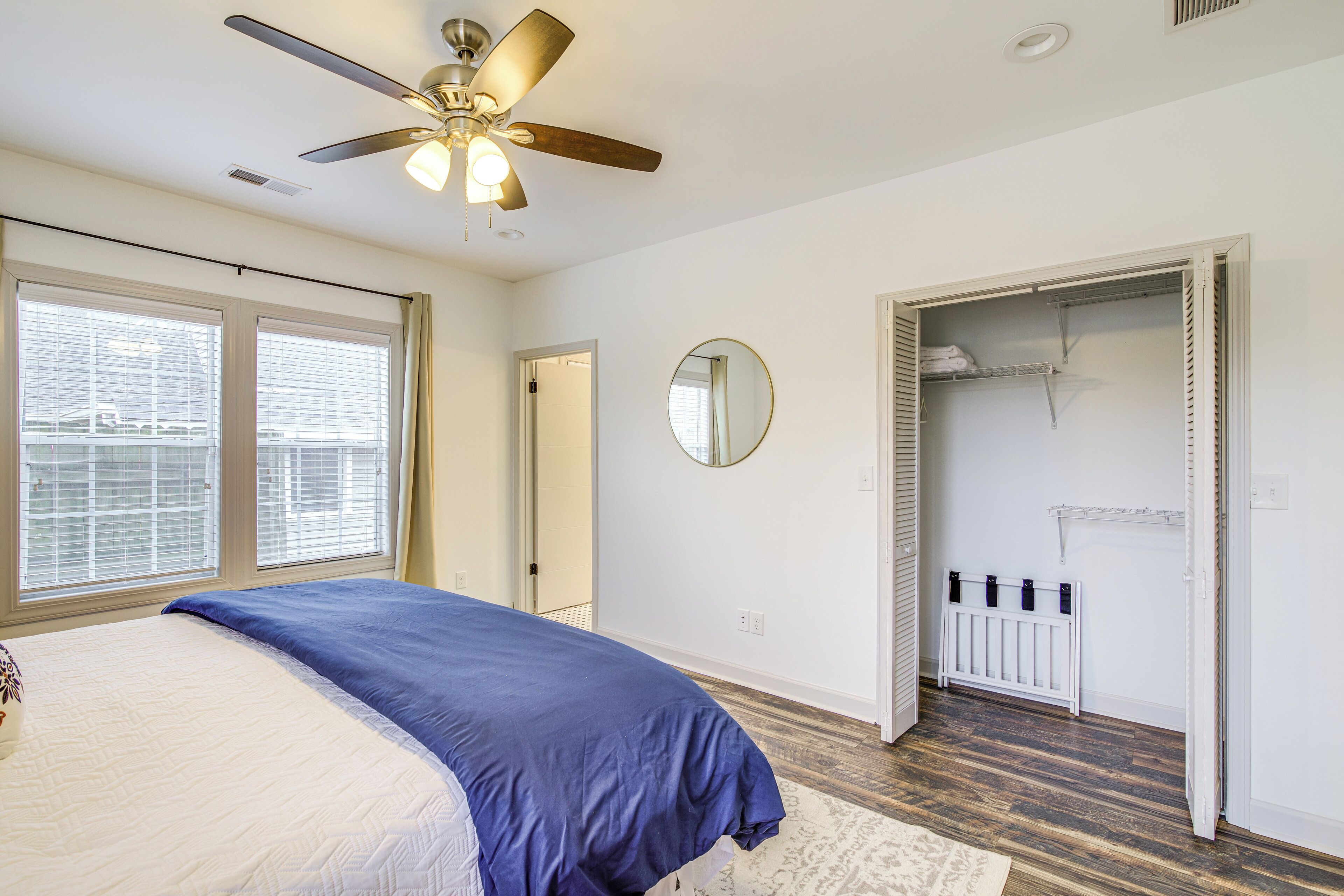 Une chambre à coucher comprenant un lit, un ventilateur de plafond, une fenêtre, un miroir et un dressing.