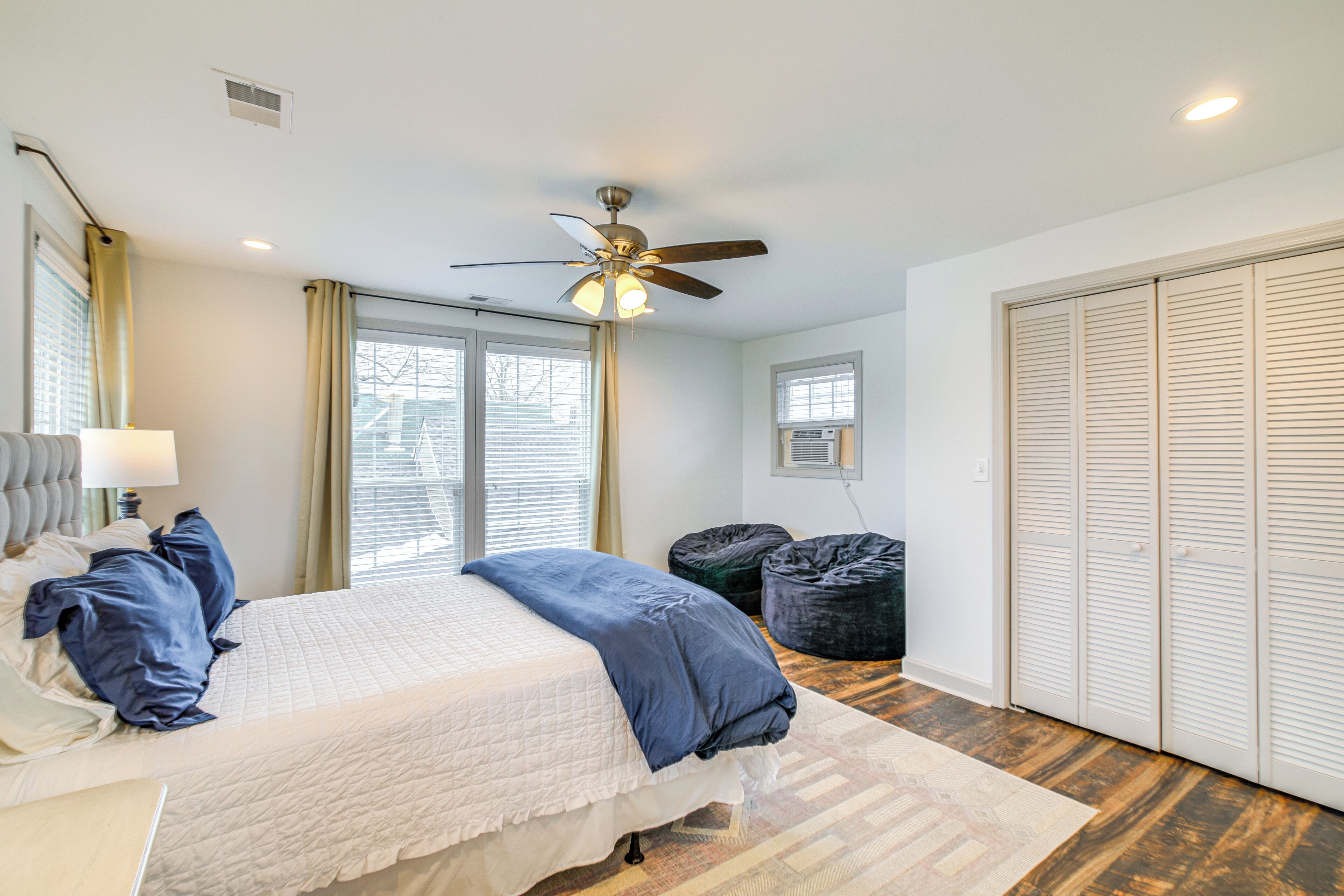 A bedroom with a bed, ceiling fan, window, air conditioning unit, and wardrobe.