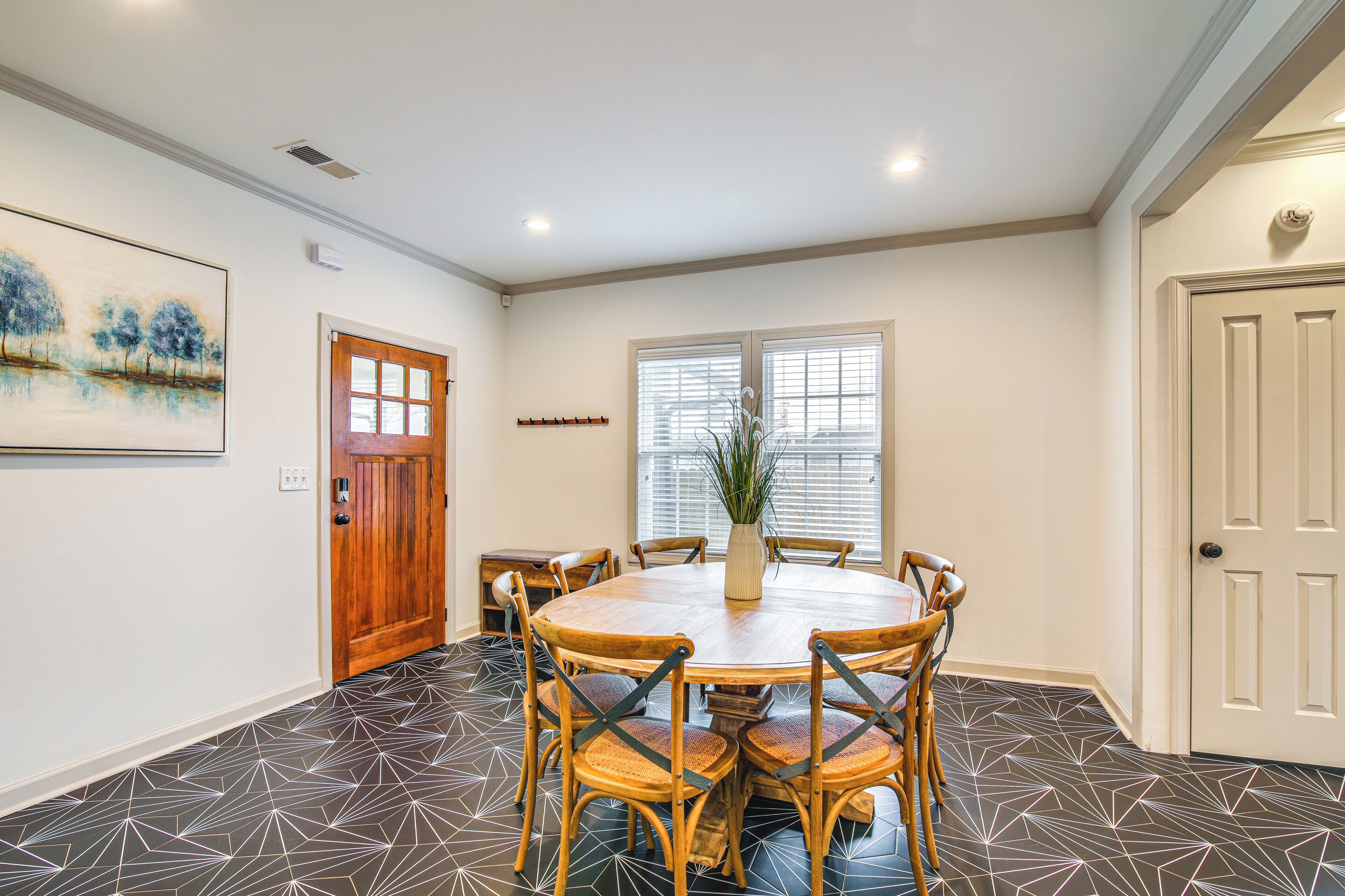 A dining area with a round wooden table and six chairs, a wooden door, and a window with blinds.