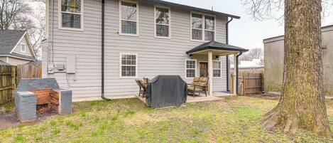 A two-story house with a covered patio area, a brick fireplace, and a large tree in the yard.