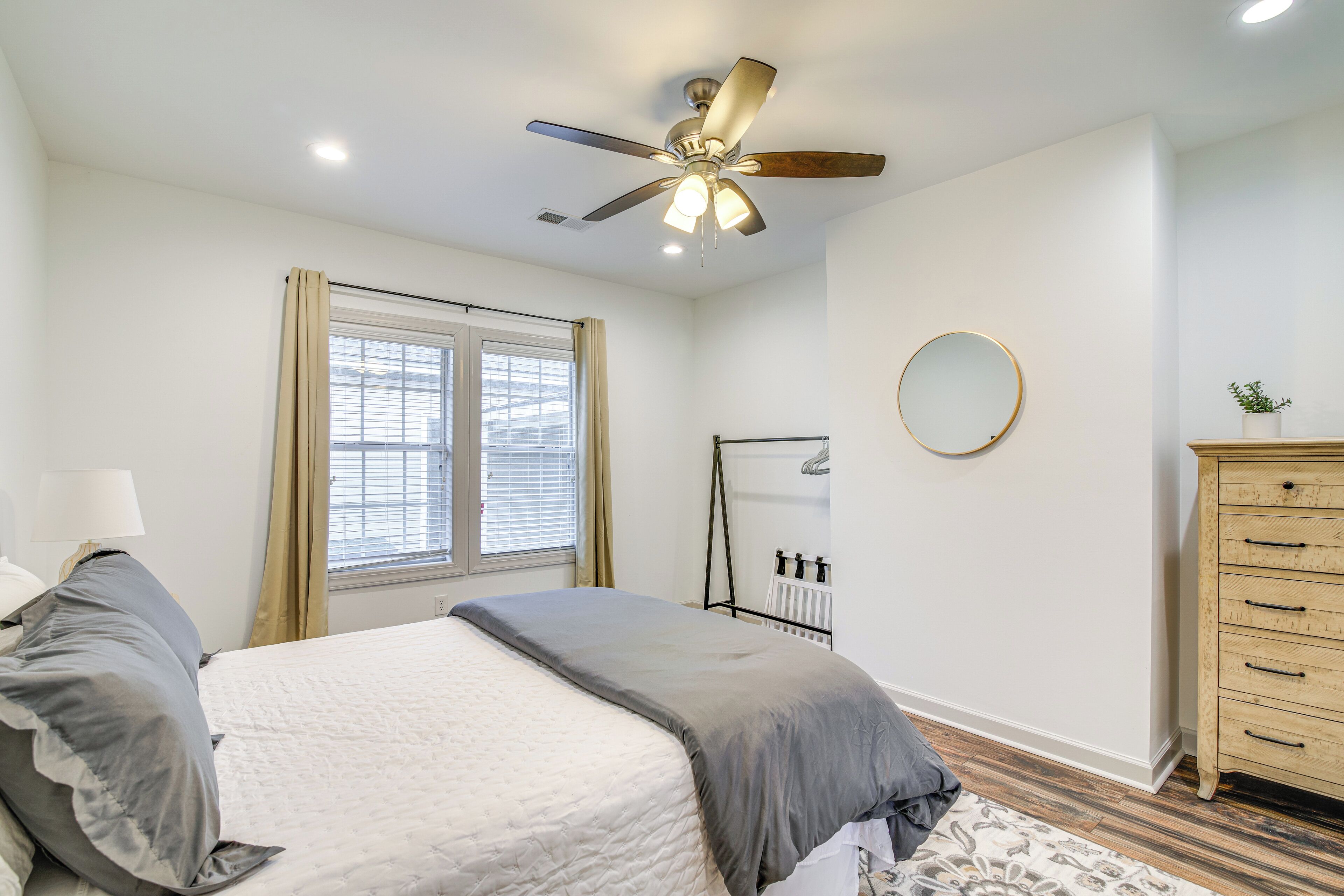 Une chambre à coucher comprenant un lit, un ventilateur de plafond, une fenêtre avec des rideaux, une commode et un radiateur.