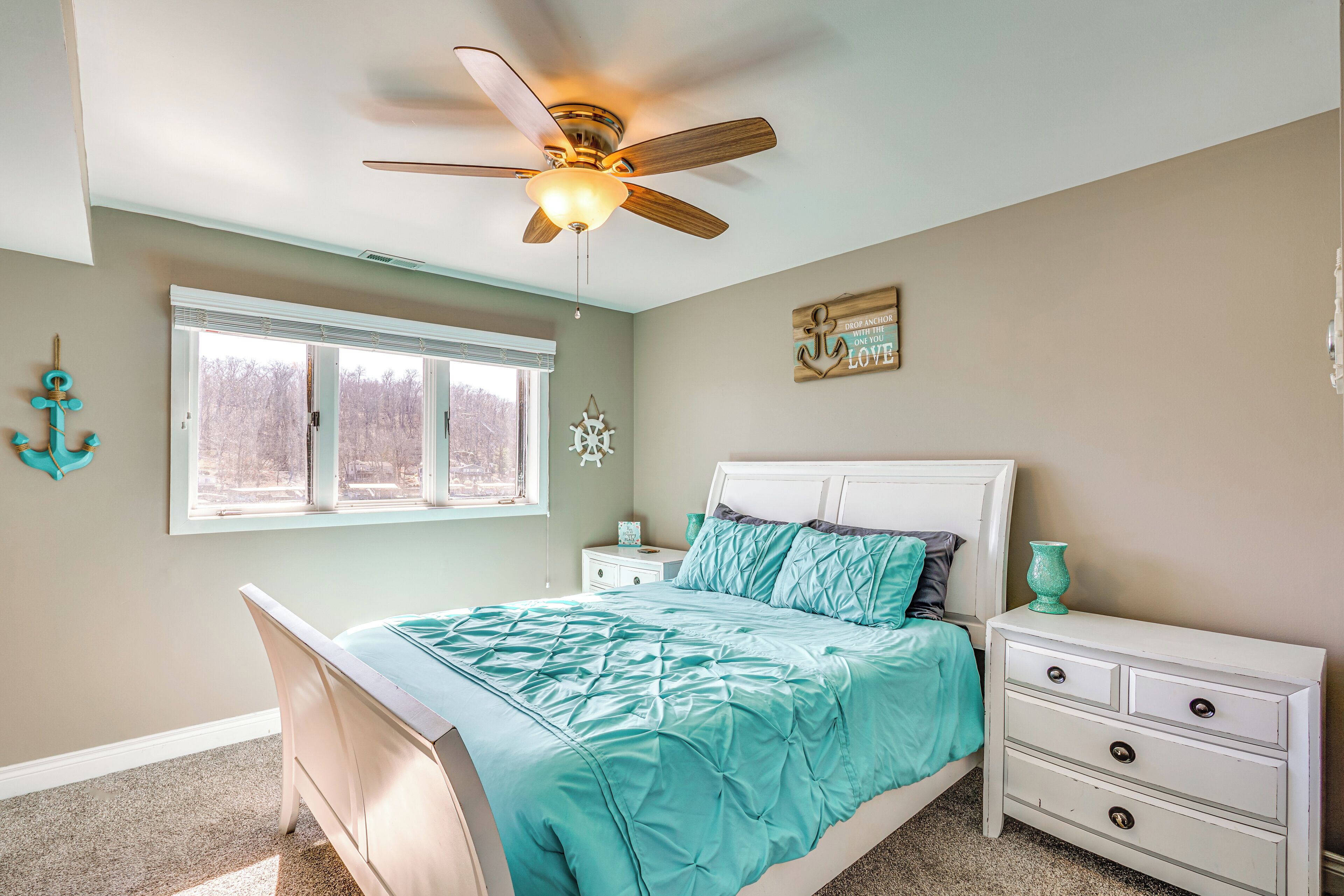 Un dormitorio con cama, mesita de noche, ventilador de techo, ventana y decoración en las paredes.