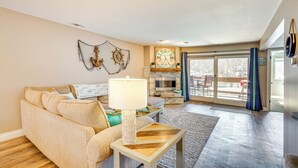 A living room with a beige sofa, a wooden coffee table, a wall clock, and a fireplace. - Osage Beach Condo Pools, Boatslip and Pickleball (Osage Beach)