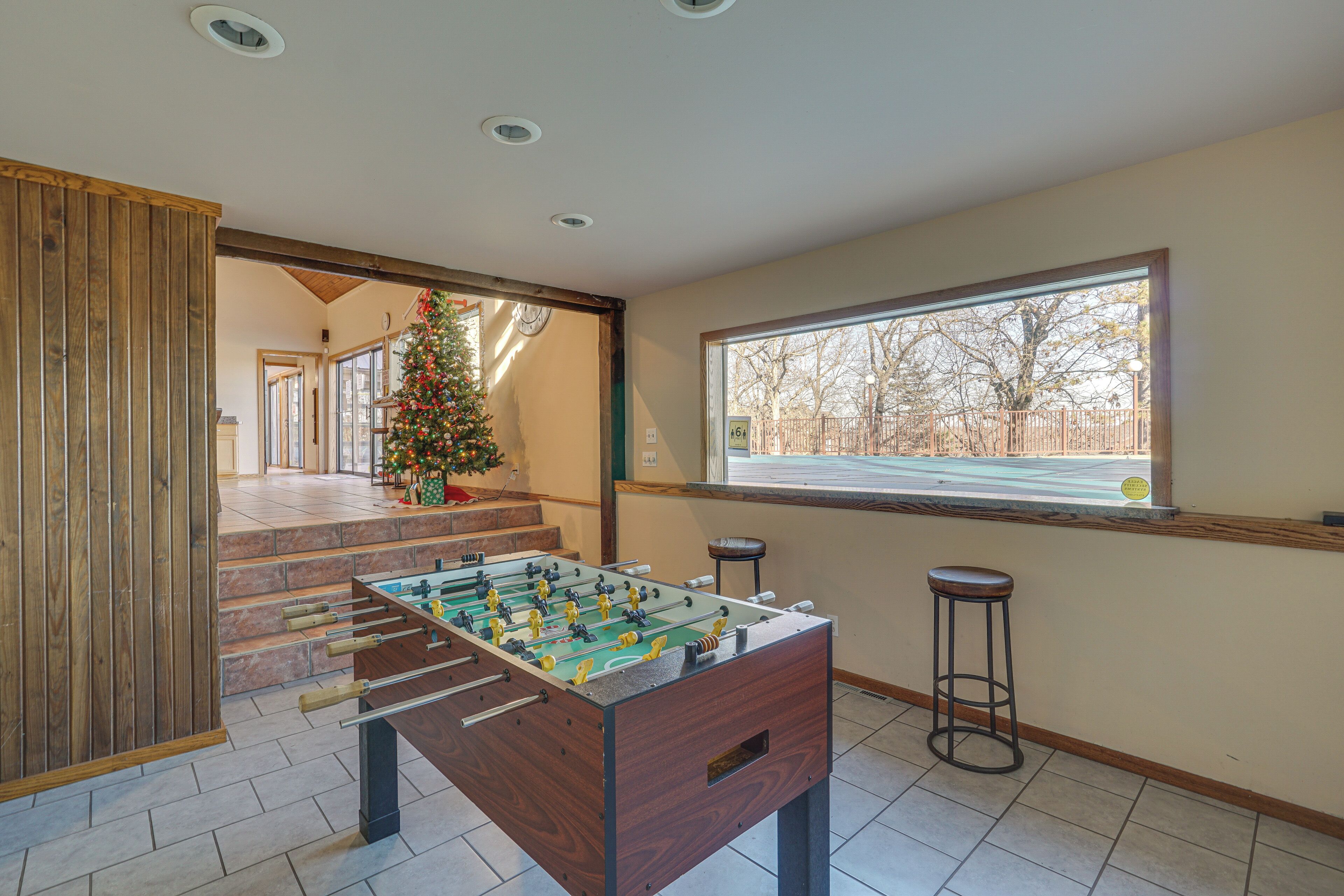 A room with a foosball table, a Christmas tree, and a window with a view of trees.