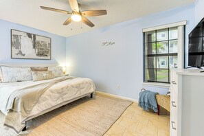 A bedroom with a bed, a ceiling fan, a window with a view, and a wall-mounted artwork.