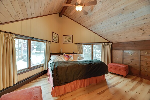 A cozy bedroom with a large bed, wooden floors, a ceiling fan, and a dresser.