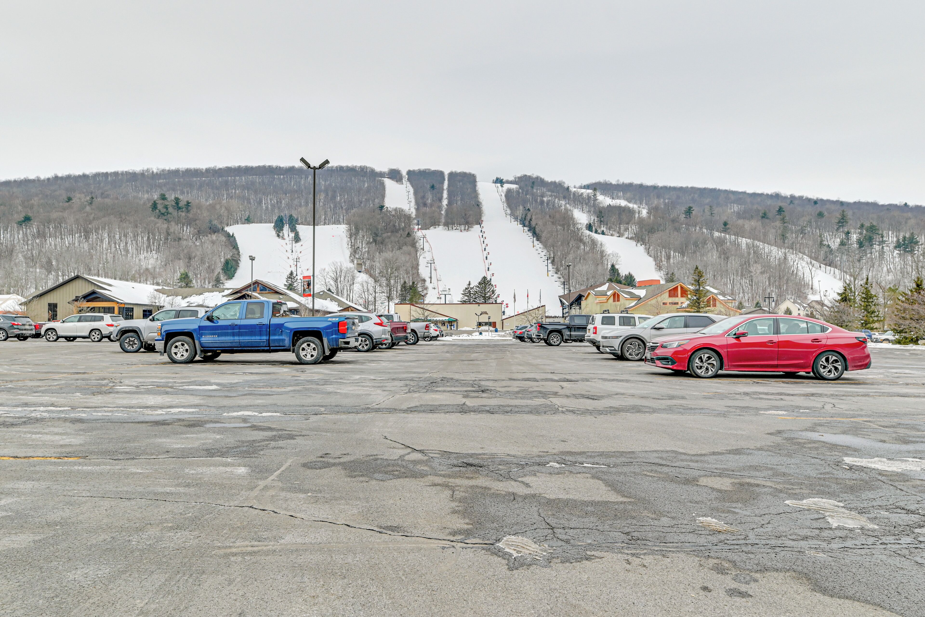 A parking lot with several vehicles, including a blue truck and a red car, in front of a building with a sloped roof.