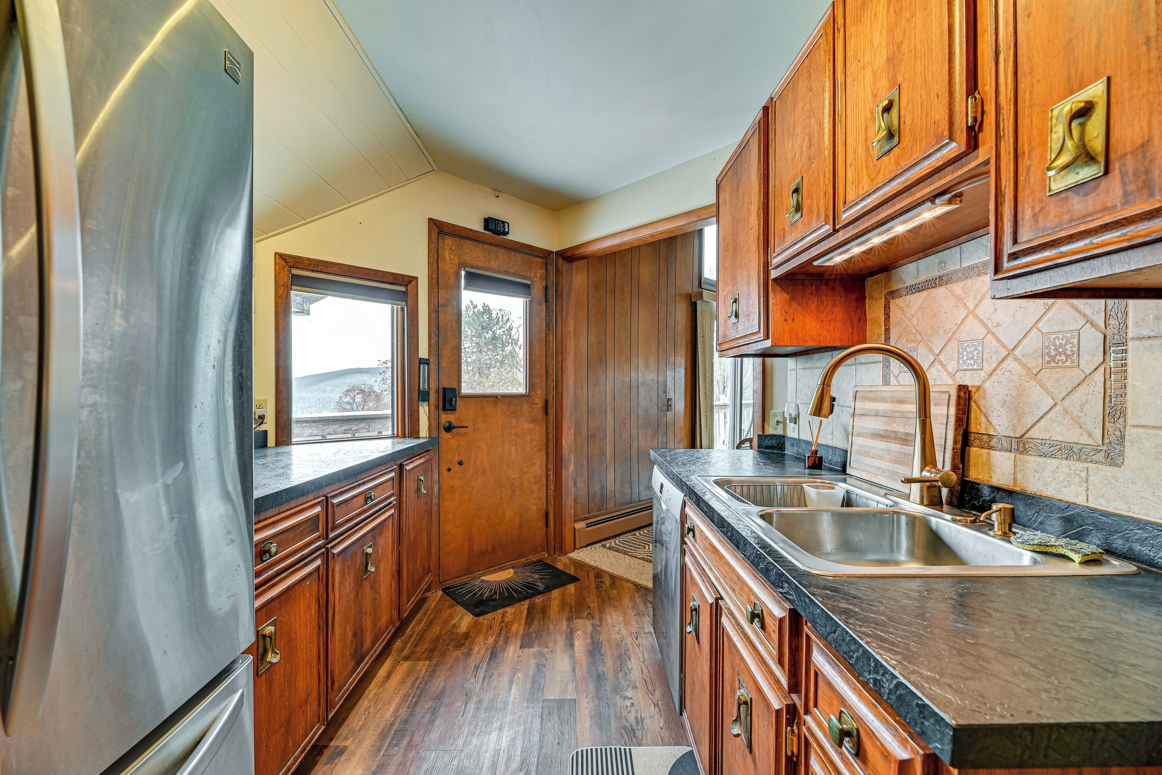 A kitchen with wooden cabinets, a stainless steel refrigerator, a sink, and a window.