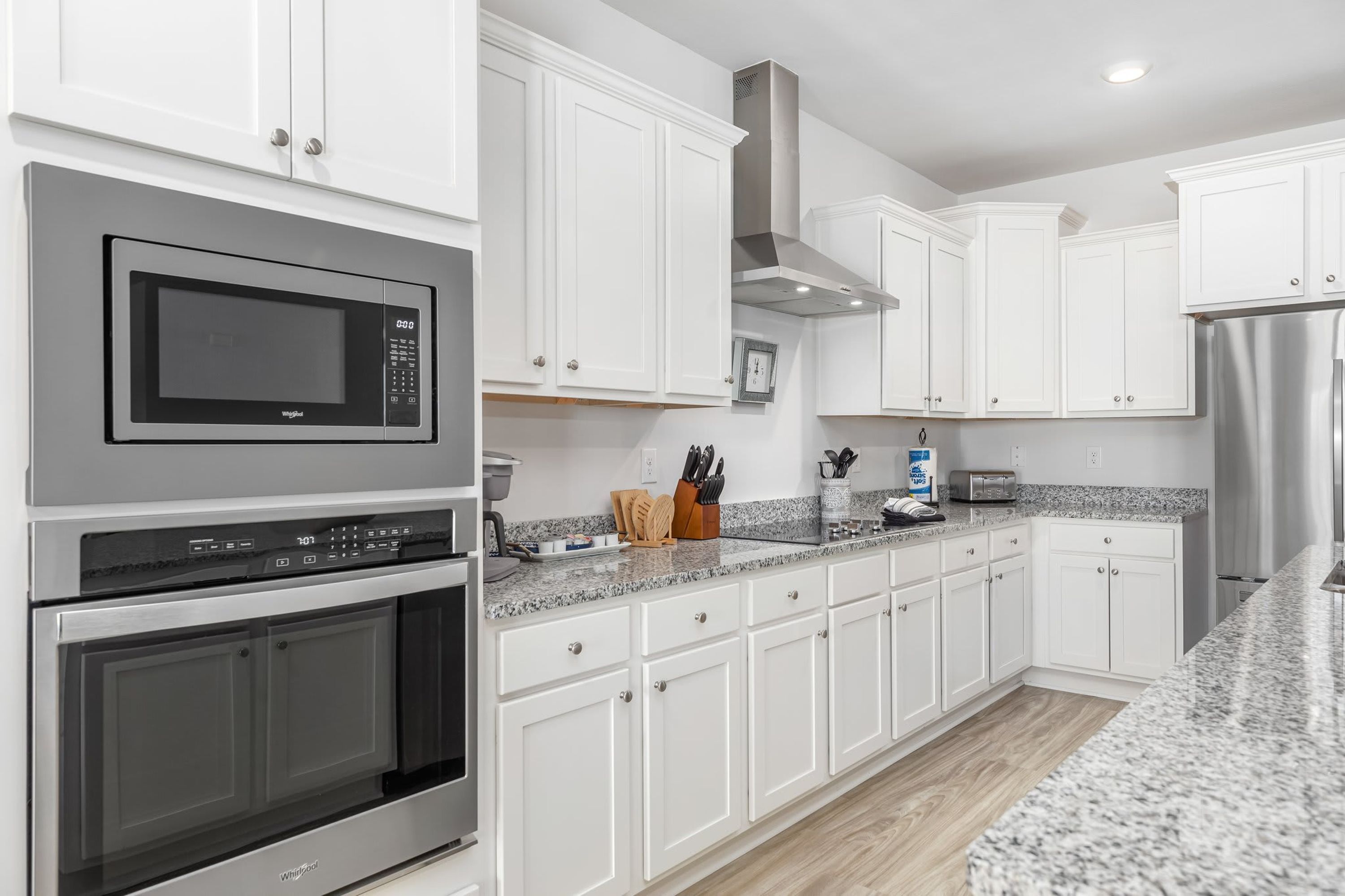 A modern kitchen with white cabinets, stainless steel appliances, granite countertops, and a built-in oven.