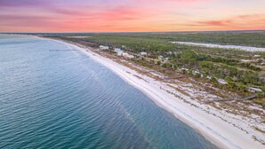 Vista aérea de una zona costera con playa, casas y un área boscosa.