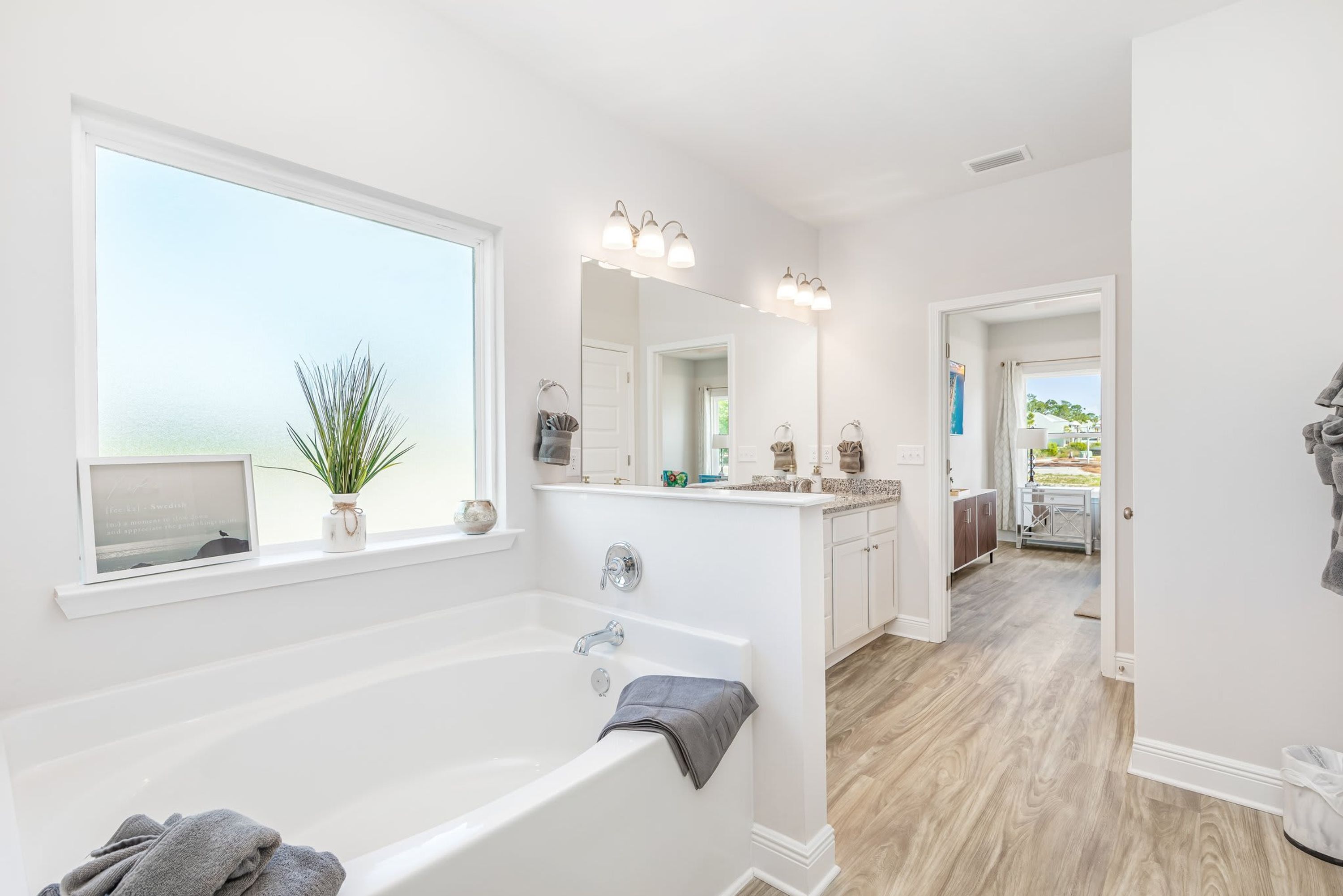 Ein modernes Badezimmer mit einer großen Badewanne, einem Waschtisch inklusive Spiegel und einem Fenster mit Blick ins Freie.