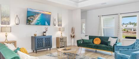 A spacious living room with a large TV, green and blue furniture, and a view of the outdoors.