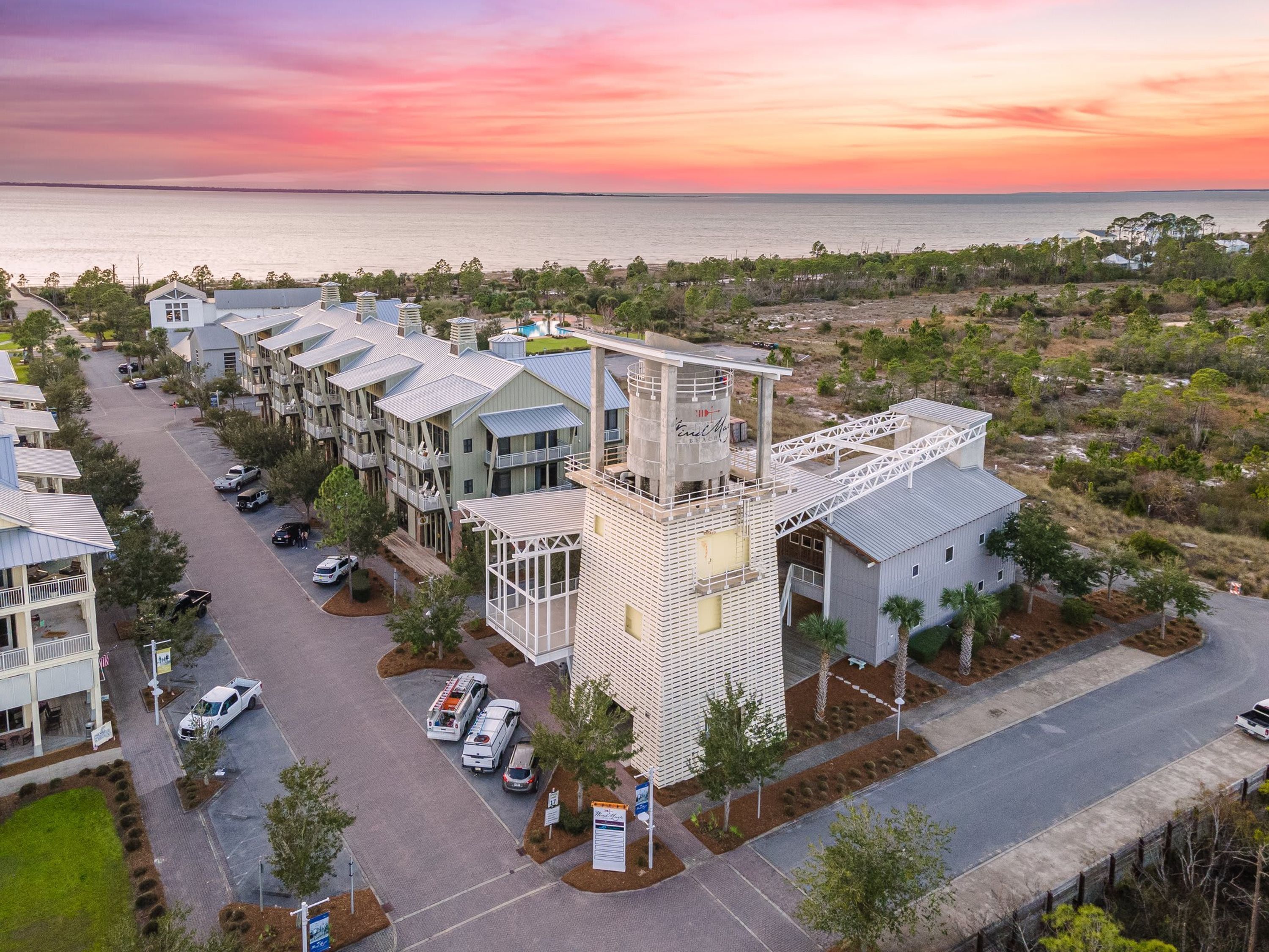A coastal hotel with multiple-story buildings, a parking area, and a view of the sea.