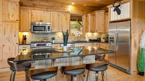 A modern kitchen with wooden cabinets, stainless steel appliances, and a central island with bar stools. - Eagle Nest Lodge Hot Tubs Mountain Views (Banner Elk)