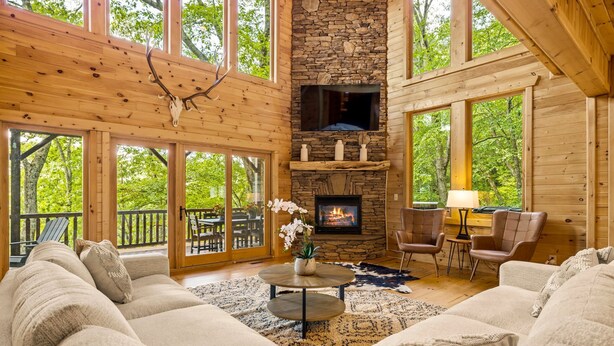 A cozy cabin interior with a stone fireplace, large windows, and a comfortable seating area. - Eagle Nest Lodge Hot Tubs Mountain Views (Banner Elk)