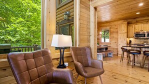 A wooden cabin interior with two leather chairs, a dining table, and a kitchen area. - Eagle Nest Lodge Hot Tubs Mountain Views (Banner Elk)