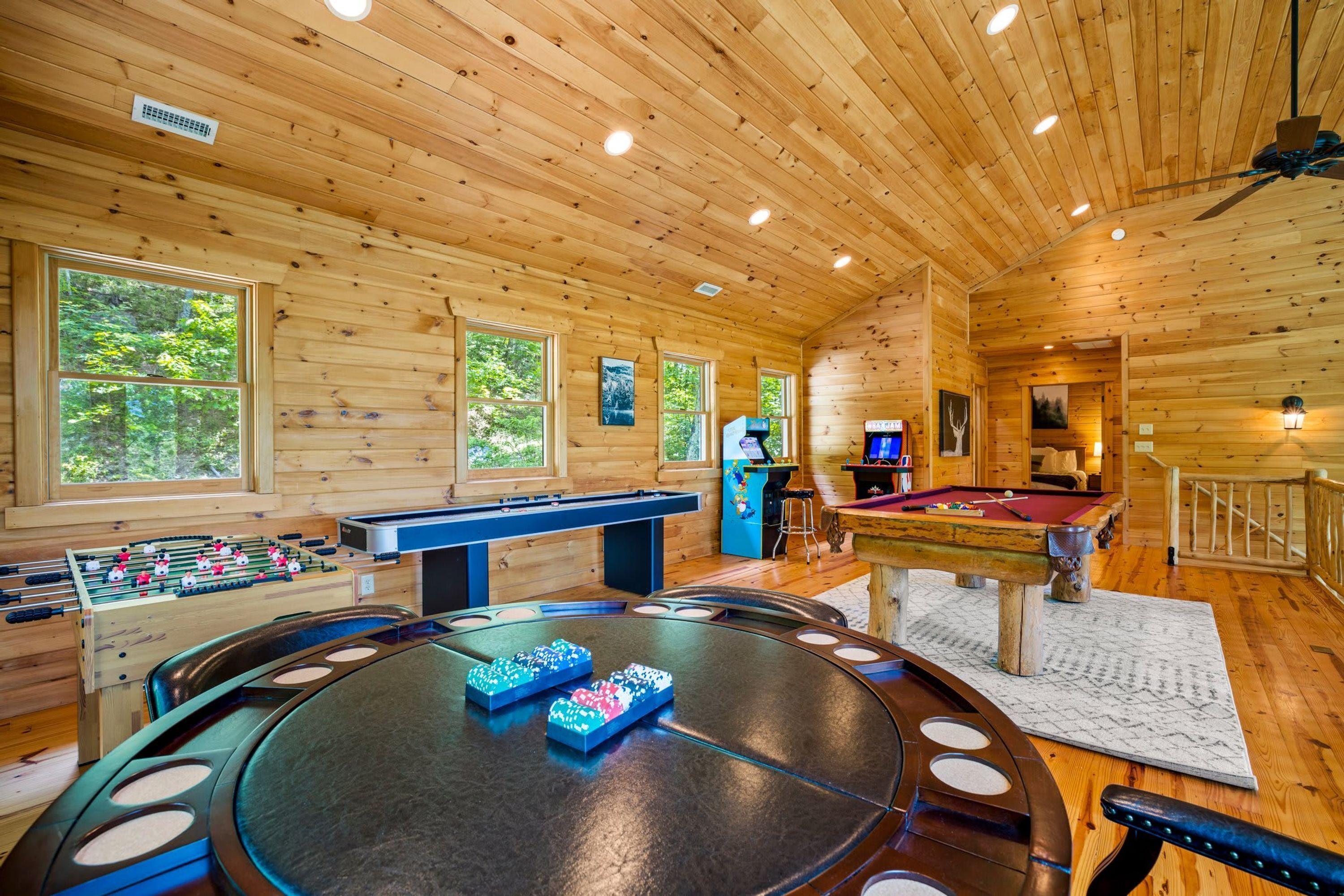A wooden-floored room with a foosball table, pool table, and a bar area.