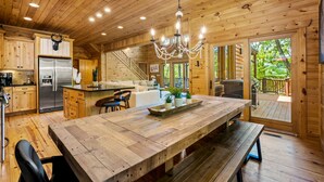 A wooden cabin interior with a large dining table, kitchen area, and a staircase leading to a deck. - Eagle Nest Lodge Hot Tubs Mountain Views (Banner Elk)